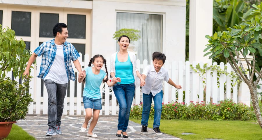 Parents and kids walking together in front of a beautiful home with a white fence